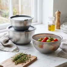 Load image into Gallery viewer, A set of stainless steel kitchen utensils, including mixing bowls and a mesh colander, displayed on a wooden shelf in a retail store.
