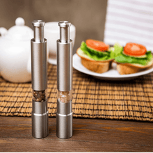 Load image into Gallery viewer, Stainless steel pepper and spice grinders on a table with fresh sandwiches in the background, showcasing adjustable coarseness.