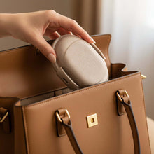 تحميل الصورة في عارض المعرض، Hand placing a beige earbud case into a brown handbag.