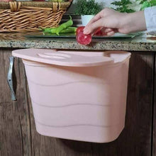 Load image into Gallery viewer, Pink wall-mounted trash bin on a kitchen counter with a hand disposing of waste.