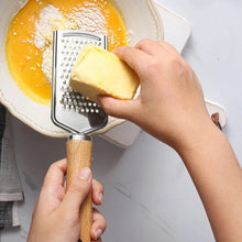 Load image into Gallery viewer, Hands using a stainless steel cheese grater with wooden handle to grate butter into a bowl of ingredients.
