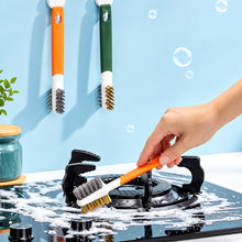 تحميل الصورة في عارض المعرض، A hand is using an orange kitchen gas stove cleaning brush with plastic scraper on a black gas stove top.