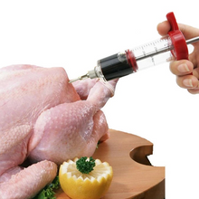 Load image into Gallery viewer, A plastic marinade injector being used to inject a liquid into a roasted chicken on a wooden cutting board, with a lemon wedge and green herb nearby.