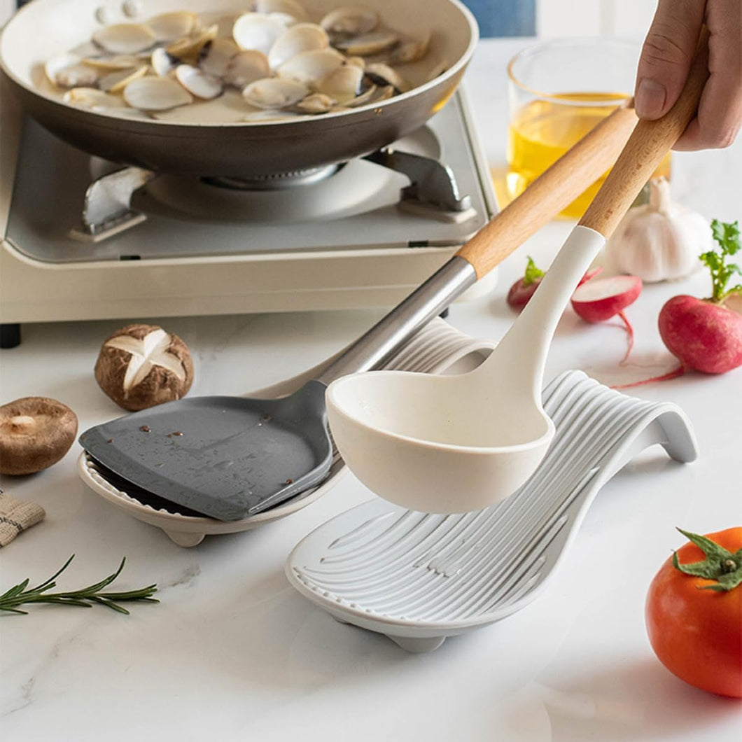 White ladle with wooden handle on a white dish rack, with cooking scene in the background.