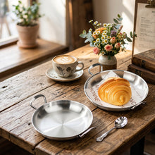 Load image into Gallery viewer, Two round stainless steel mini pans with loop handles on a glossy black surface, with one pan containing a croissant on white paper liner and the other empty.
