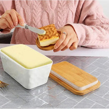 Load image into Gallery viewer, Person using a knife to spread butter from a white porcelain butter dish with bamboo lid on a table.
