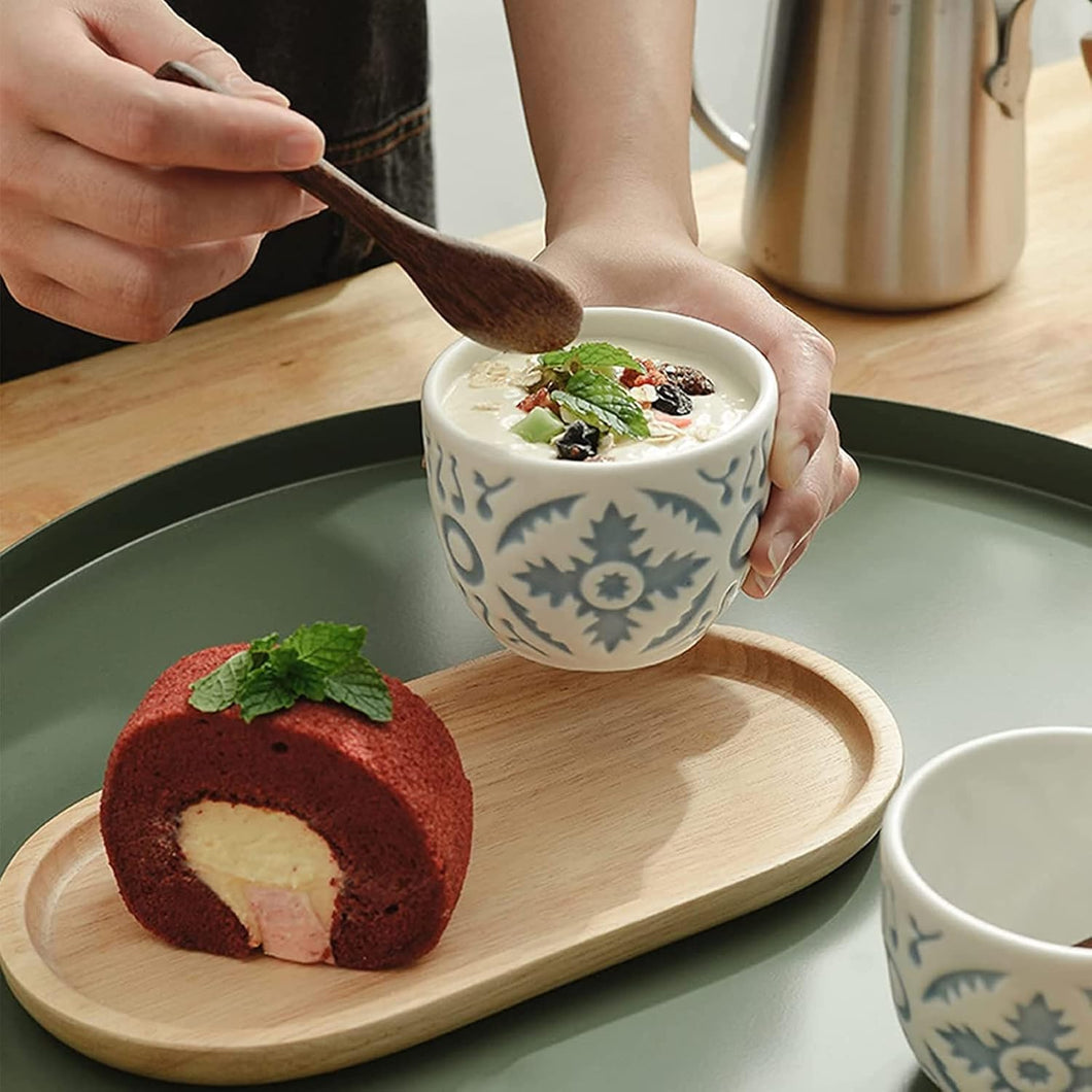 Person holding a bowl of dessert with a red velvet roll cake on a wooden tray.