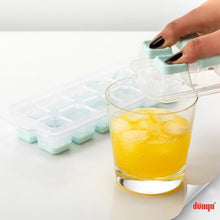 Load image into Gallery viewer, Hand using a silicone ice cube tray to fill a glass with yellow liquid on a white background.
