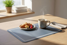 تحميل الصورة في عارض المعرض، A dark slate blue rectangular mouse pad with rounded corners, featuring a double white border and a small white line-art lamp illustration near the top right, shown on a light wood desk.
