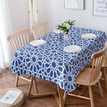 Load image into Gallery viewer, Dining table with a blue geometric patterned tablecloth, surrounded by wooden chairs.

