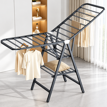 Load image into Gallery viewer, Dark grey three-tier drying rack with wings open, holding clothes in a room
