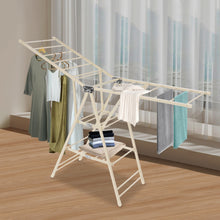 Load image into Gallery viewer, Foldable clothes drying rack with clothes on a wooden floor near a window.
