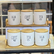 Load image into Gallery viewer, Set of five white canisters with wooden lids labeled for sugar, coffee, and tea on a wooden stand.

