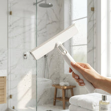 Load image into Gallery viewer, A white plastic T-shaped squeegee with a gray rubber blade, resting on a textured off-white fabric surface.
