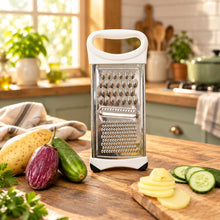 تحميل الصورة في عارض المعرض، A white and stainless steel manual box grater with a handle, standing upright on a white surface. To the left are whole potatoes and a cucumber, and to the right is a wooden cutting board with sliced potatoes and cucumbers.
