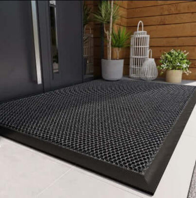 Black textured mat on a white floor with a wooden wall and plants in the background