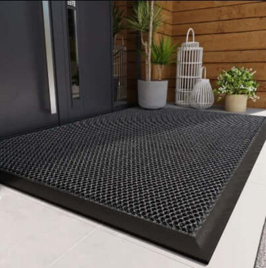 Black textured mat on a white floor with a wooden wall and plants in the background