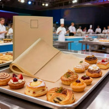 Load image into Gallery viewer, A metal baking tray filled with assorted pastries and tarts, set in a bakery or kitchen environment with a large kraft paper envelope standing behind it.
