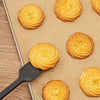 Golden spiral-shaped cookies on a parchment baking sheet, with one being lifted by a black spatula on a wooden surface.