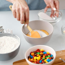 تحميل الصورة في عارض المعرض، Person mixing ingredients in a bowl with colorful candies on a kitchen counter.
