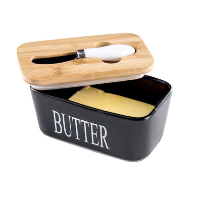 Black porcelain butter dish with bamboo lid and spreader, holding two sticks of butter.