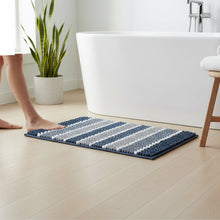 تحميل الصورة في عارض المعرض، Striped bath mat on a wooden floor with a basket of towels and slippers in the background.
