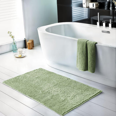 Green bath mat on a white bathroom floor with a white bathtub and green towels.
