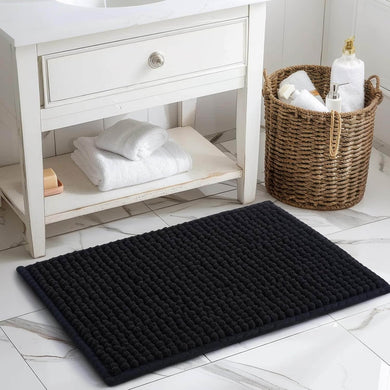 Black bath mat on a bathroom floor with a white cabinet and basket in the background.