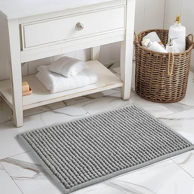 Gray textured bath mat on a bathroom floor with a white cabinet and basket in the background.