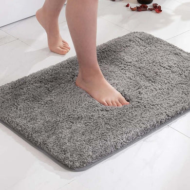 Gray bath mat on a white tiled floor with feet stepping onto it.