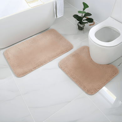 Beige bath mats on a bathroom floor with a toilet and plant in the background.