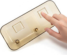 تحميل الصورة في عارض المعرض، A translucent beige plastic dual switch cover plate with a human hand pressing one of the square switches, shown against a plain white background.
