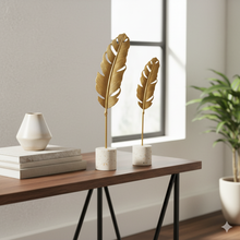 تحميل الصورة في عارض المعرض، Decorative gold feather sculptures on a wooden table with a vase and books.
