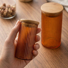 تحميل الصورة في عارض المعرض، Brown ribbed glass container with wooden lid held by a hand on a wooden surface.
