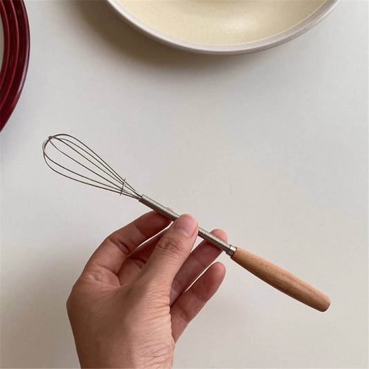 Hand holding a mini whisk with wooden handle