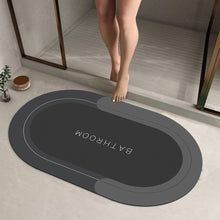 Load image into Gallery viewer, Gray bath mat with &#39;Bathroom&#39; text on a bathroom floor.
