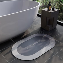 Load image into Gallery viewer, Gray bath mat with &#39;Bathroom&#39; text on a tiled floor next to a freestanding bathtub.
