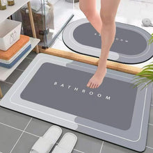 Load image into Gallery viewer, Gray bath mat with &#39;Bathroom&#39; text on a tiled floor, person stepping onto it.
