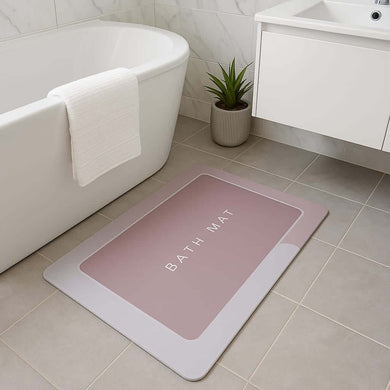 Pink bath mat with 'Bath Mat' text on a tiled bathroom floor.