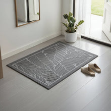 تحميل الصورة في عارض المعرض، Gray doormat with leaf pattern on a light wooden floor, next to a plant and shoes.

