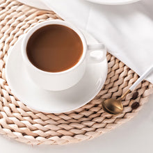 Load image into Gallery viewer, White cup of coffee on a woven placemat with a gold spoon
