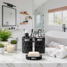 Load image into Gallery viewer, A bathroom accessory set featuring a textured black soap dispenser, matching cup, and a small round container with a lid, shown in front of a blurred modern bathroom background.
