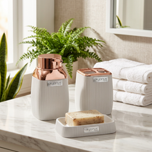 Load image into Gallery viewer, A set of three bathroom accessories with copper frames, including a liquid soap dispenser, a toothbrush and paste cup, and a dry soap dispenser, all in a beige color.
