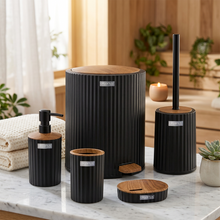 تحميل الصورة في عارض المعرض، A 5-piece bathroom vanity set in black ribbed ceramic with natural wood tops, including a foot caddy, toilet holder with handle, soap dispenser, cup, and lid, shown on a white reflective surface with a blurred kitchen background.
