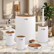 تحميل الصورة في عارض المعرض، A coordinated bathroom accessory set in white ribbed ceramic with light wood lids, arranged on a marble surface in a bright bathroom. The set includes a tall trash can with lid, toilet brush holder with stick, soap dispenser, small canisters, a tray with bar of soap, and a small footed container.
