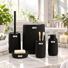Load image into Gallery viewer, A bathroom set of black ribbed ceramic containers including a toilet brush holder, soap dish with bar of soap, toothbrush holder, and two smaller storage jars, shown in front of a softly blurred modern bathroom background.
