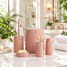 Load image into Gallery viewer, A coordinated bathroom accessory set in a dusty pink ribbed finish, including a tall toilet brush holder with a matching handle, a large cylindrical container, a toothbrush holder, a small cup, a soap dish with a bar of soap, and a smaller cylindrical container, displayed in front of a softly blurred modern bathroom interior.
