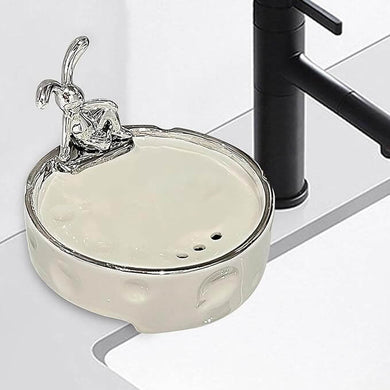 Elegant porcelain soap holder with drainage, featuring a silver-glazed finish, placed beside a modern faucet in a bathroom.