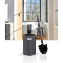 Load image into Gallery viewer, A dark gray toilet brush with a black bristle head and a long handle, shown standing next to its matching dark gray cylindrical holder on a white surface. The background features a blurred interior bathroom scene with a window.
