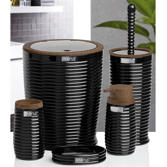 A coordinated bathroom accessory set in glossy black ribbed ceramic with light brown wood tops, including a tall lidded canister, a smaller canister, a pump bottle, a brush holder, a lid, and a standing brush, shown on a white surface with a softly blurred interior background.
